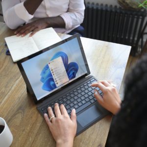 Overhead view of two people at a table working with a Microsoft laptop and notebook